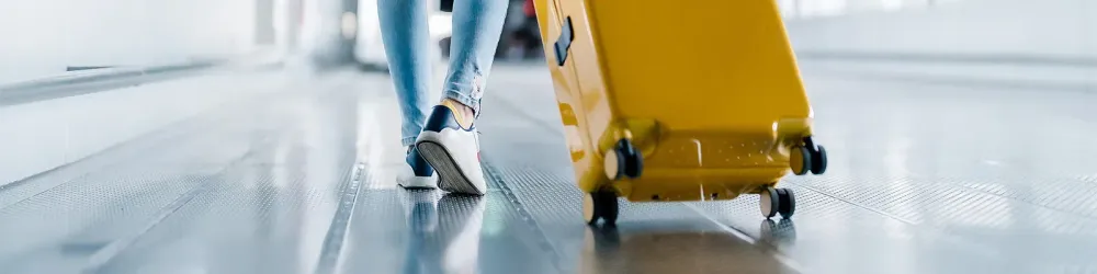 Close up of a person's legs and feet as they walk through the airport pulling a yellow suitcase